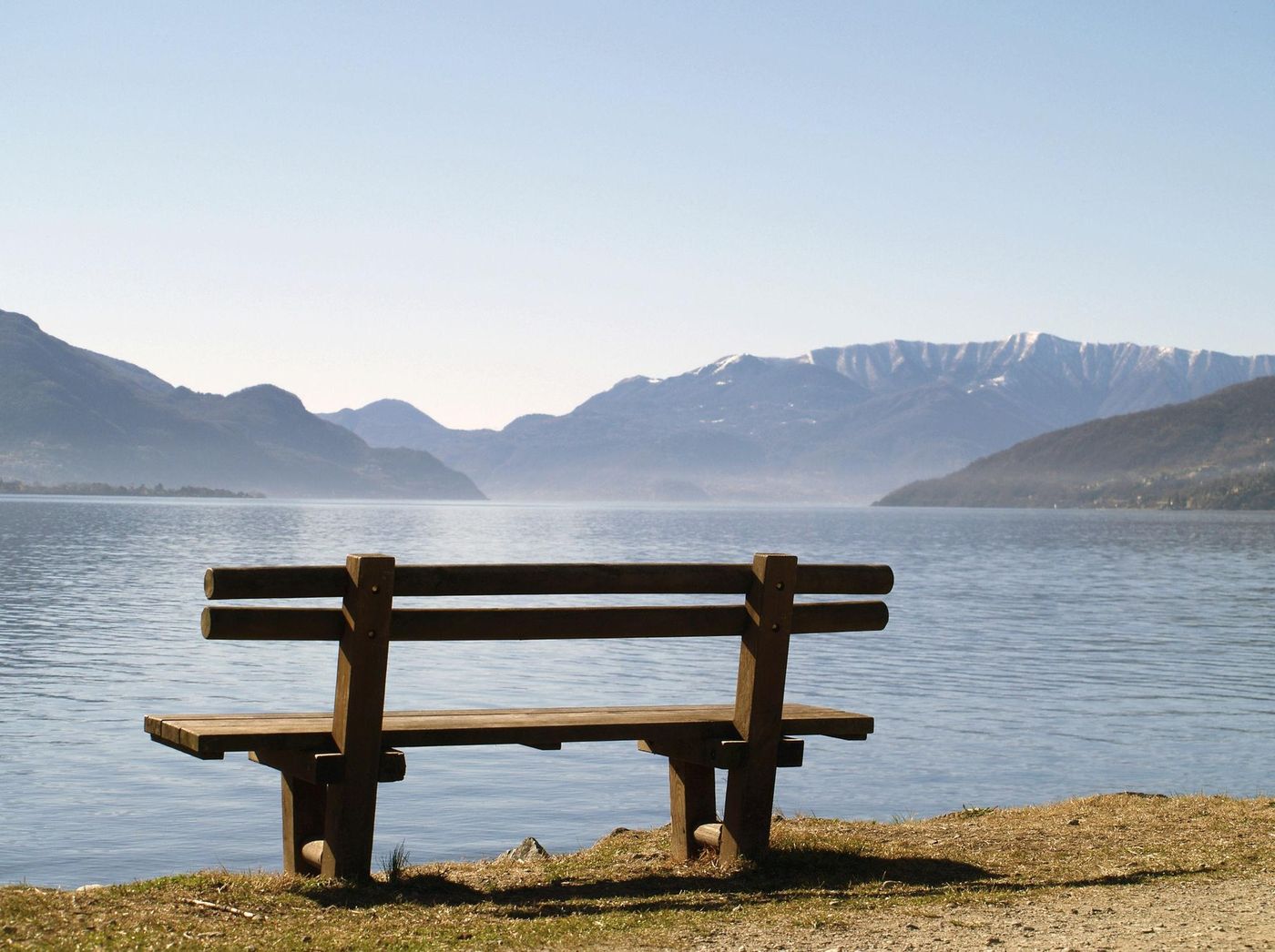 Eine Holzbank am Ufer eines stillen Sees vor Bergen